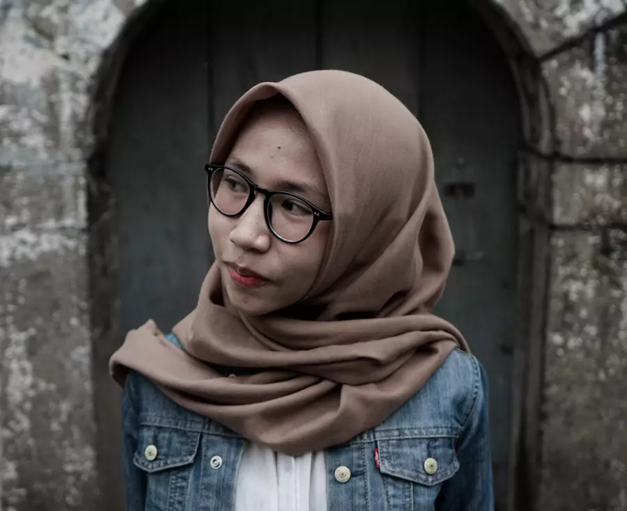 A woman wearing a headscarf smiles while looking down a street